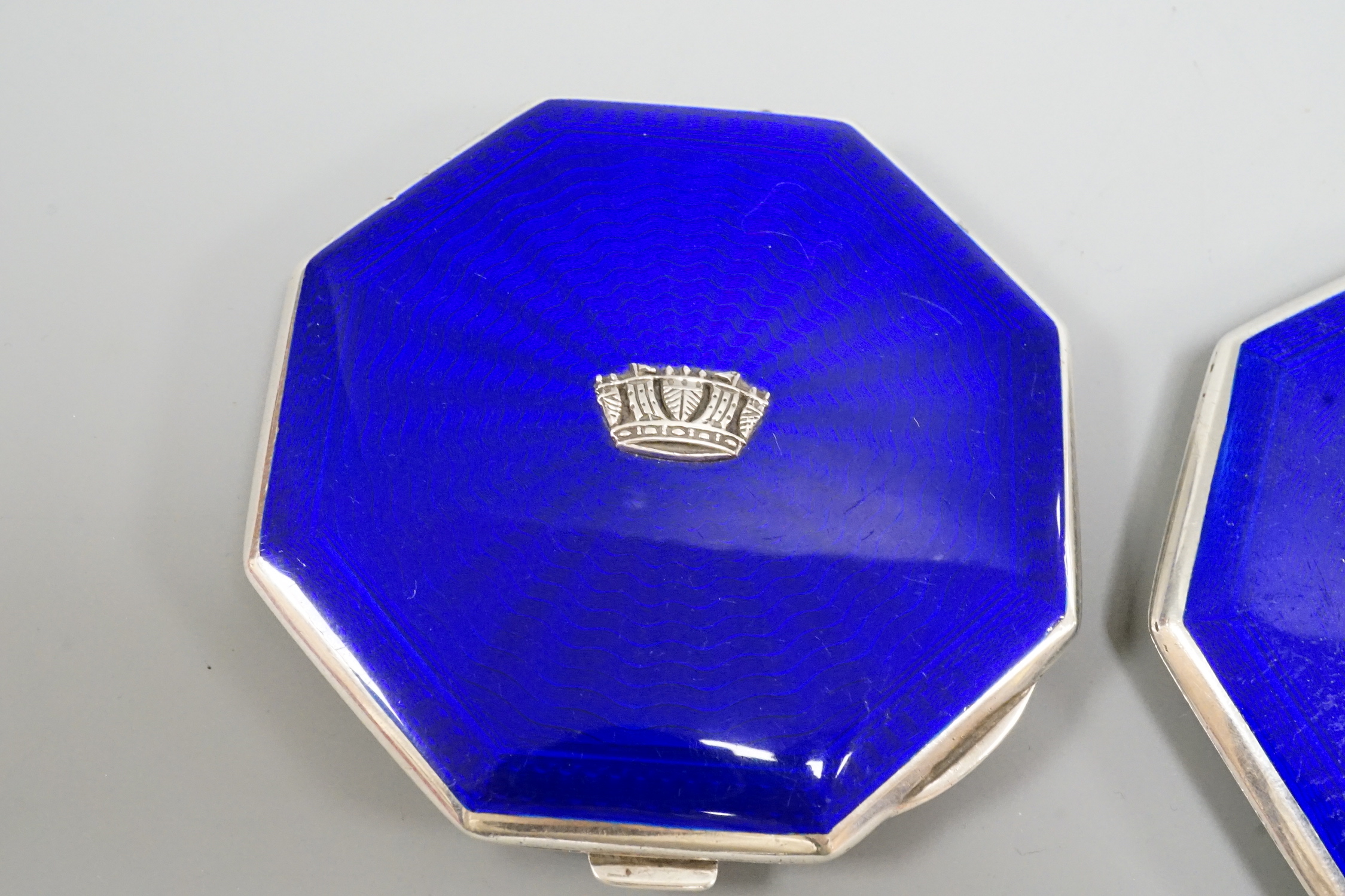 A pair of George VI part engine turned silver and enamel octagonal compacts, with coronet appliqués, John William Barrett, Birmingham, 1941, 77mm.